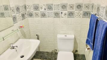 A bathroom with a white sink, toilet, and shower. The walls have patterned tiles.
