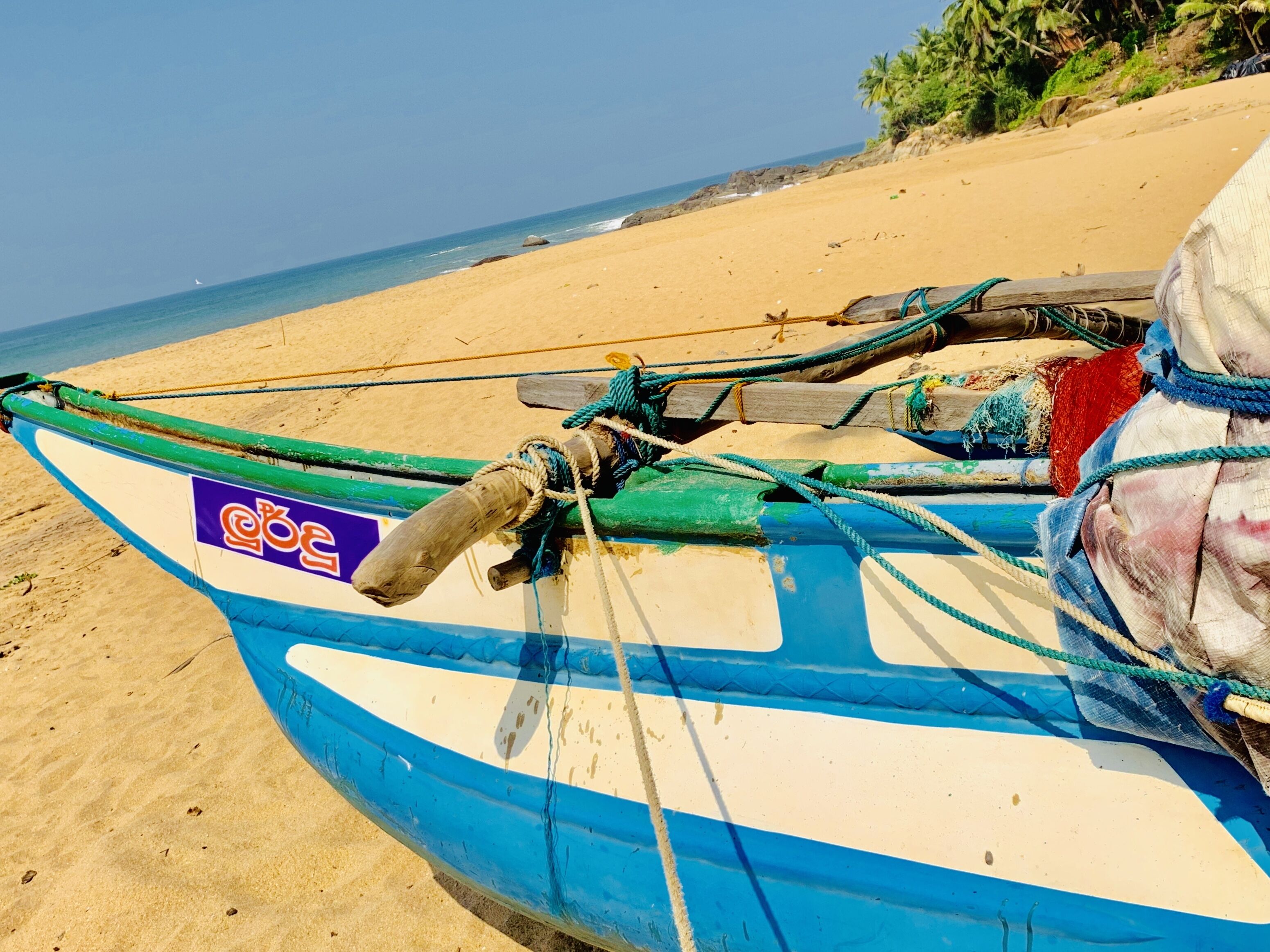Ein Boot mit festgebundenen Seilen liegt auf einem sandigen Strand, im Hintergrund das Meer.