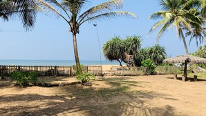 Une plage de sable bordée de palmiers, avec une clôture en bois et une structure surmontée d’un toit de chaume.