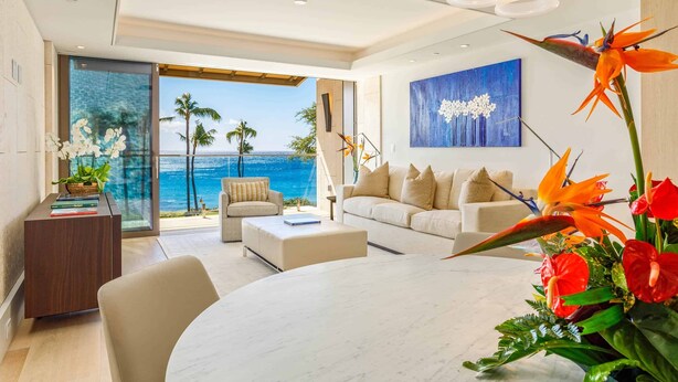 A modern living room with a view of the ocean, a dining area, and a large artwork on the wall.
