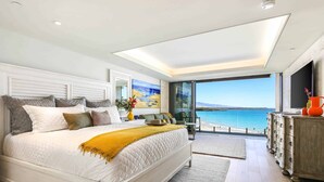 A bedroom with a large bed, a view of the sea, a wooden dresser, and a balcony.