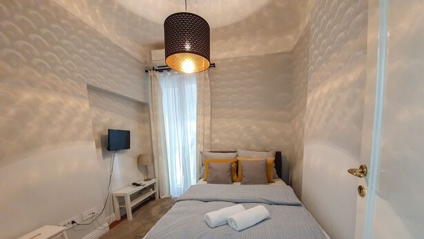 A bedroom with a bed, a bedside table, a lamp, a TV mounted on the wall, and a door. - Srecko Centar Apartment (Belgrade)