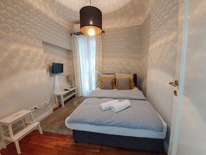 Un dormitorio con cama, mesita de noche, lámpara, televisor montado en la pared y una puerta.
