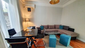 A modern living room with a wooden floor, a glass dining table, a sofa, and blue accent chairs. - Srecko Centar Apartment (Belgrade)