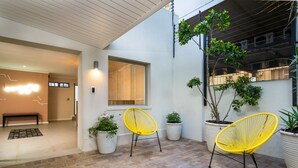 A modern patio with two yellow chairs, potted plants, and a bench.