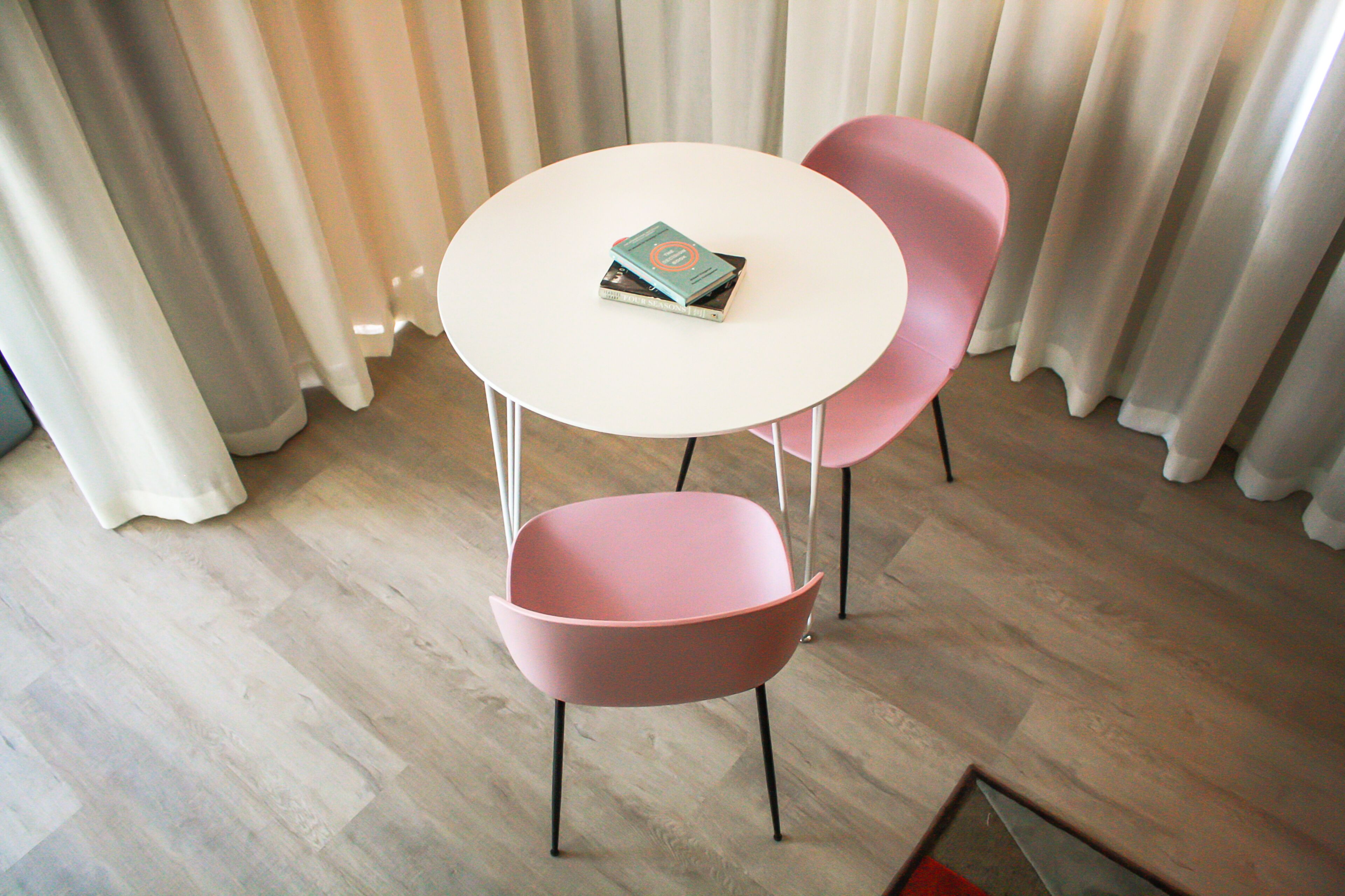 Ein Zimmer mit einem runden weißen Tisch und zwei rosafarbenen Stühlen, ein Buch auf dem Tisch und ein Holzboden.