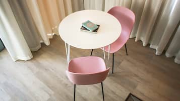 A room with a round white table and two pink chairs, a book on the table, and a wooden floor.