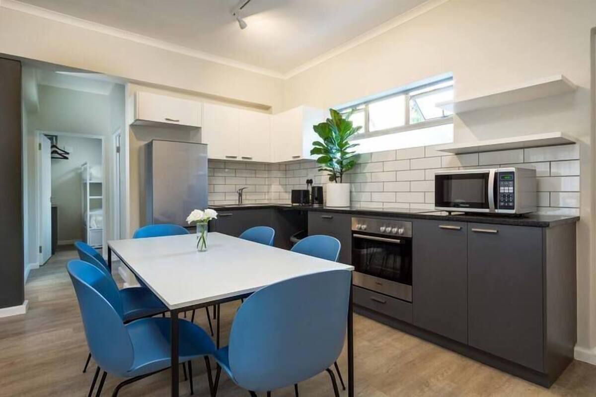 A modern kitchen with grey cabinets, a white countertop, a microwave, and a dining area with blue chairs and a white table.