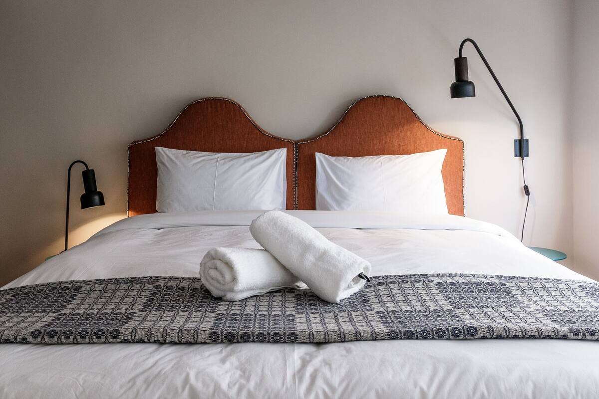 A neatly made bed with white linens, a rolled towel, and a patterned throw.