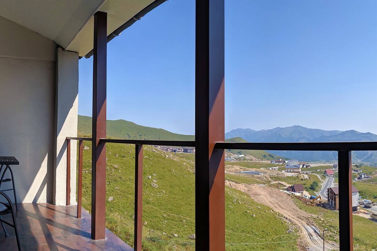 Ein Balkon mit Tisch und Stühlen mit Blick auf eine ländliche Landschaft, einschließlich Gebäude und Hügel.