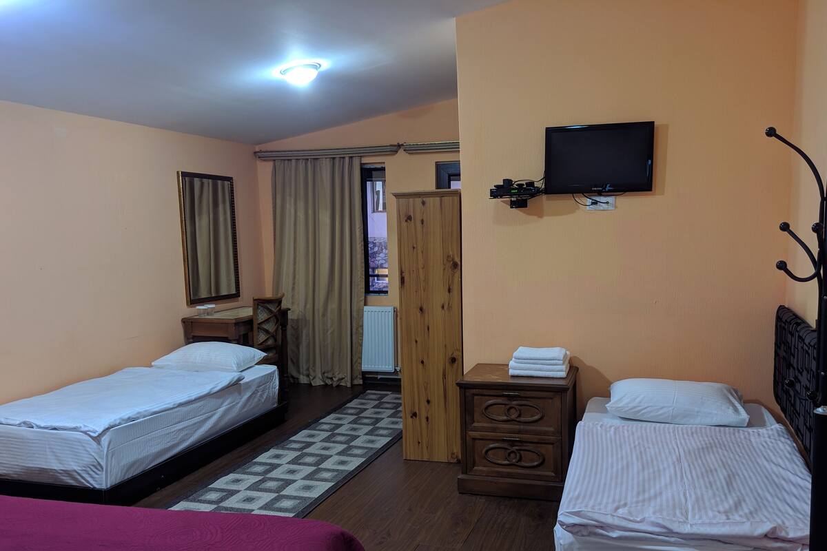 Ein Hotelzimmer mit zwei Einzelbetten, einem Holzschrank, einem kleinen Tisch mit Lampe, einem an der Wand befestigten Fernseher und einem gemusterten Teppich.