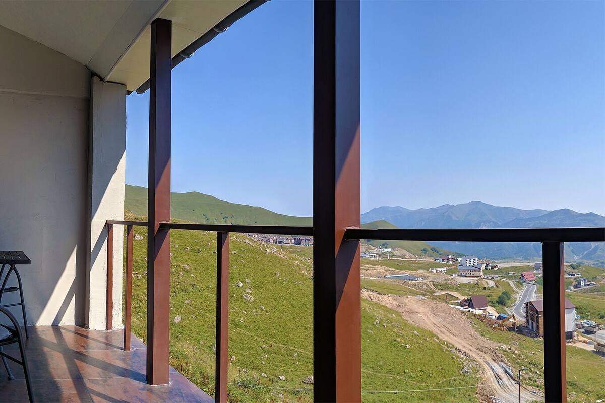 Ein Balkon mit Tisch und Stühlen, der auf eine ländliche Landschaft mit Gebäuden und Hügeln blickt.