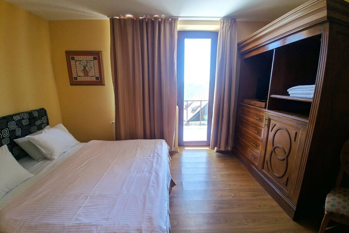 Ein Hotelzimmer mit einem Bett, einem Schminktisch, einem Fenster mit Vorhängen und einem gerahmten Bild an der Wand.