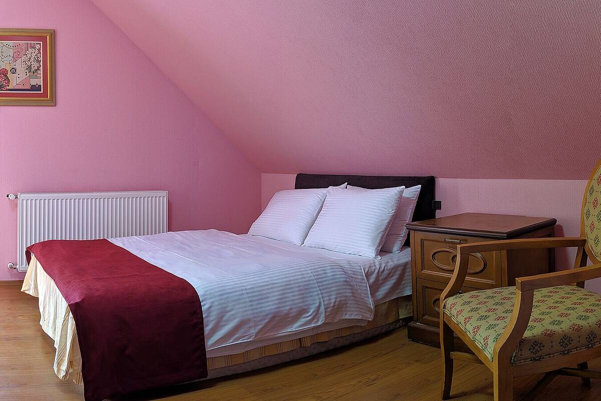 Ein Schlafzimmer mit einem Bett, einem Holzstuhl, einem Nachttisch und einer Heizung.