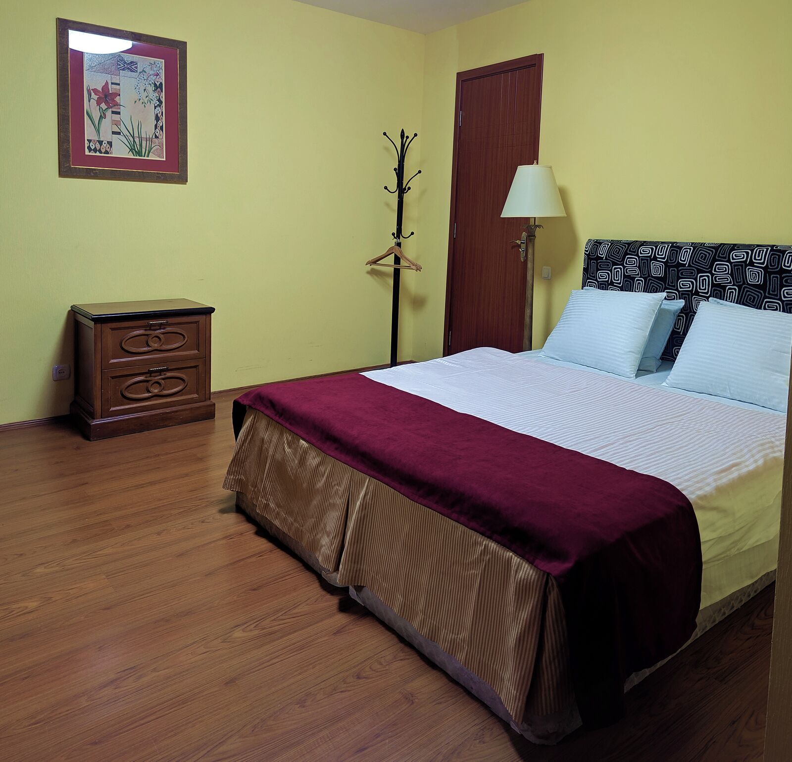Une chambre à coucher avec un lit, une table de chevet, une lampe et un porte-manteau.