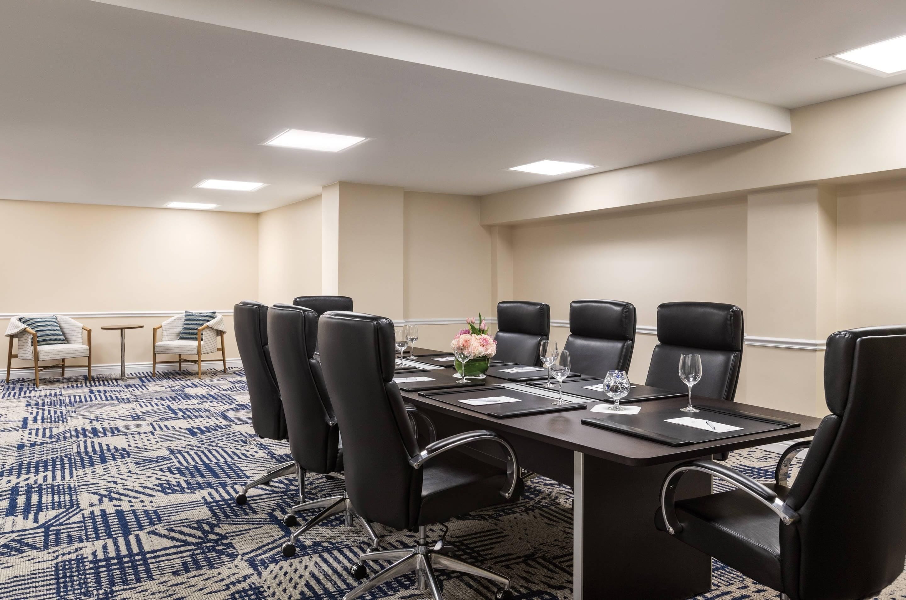 Un salón de conferencias con una larga mesa, sillas negras y una alfombra estampada.
