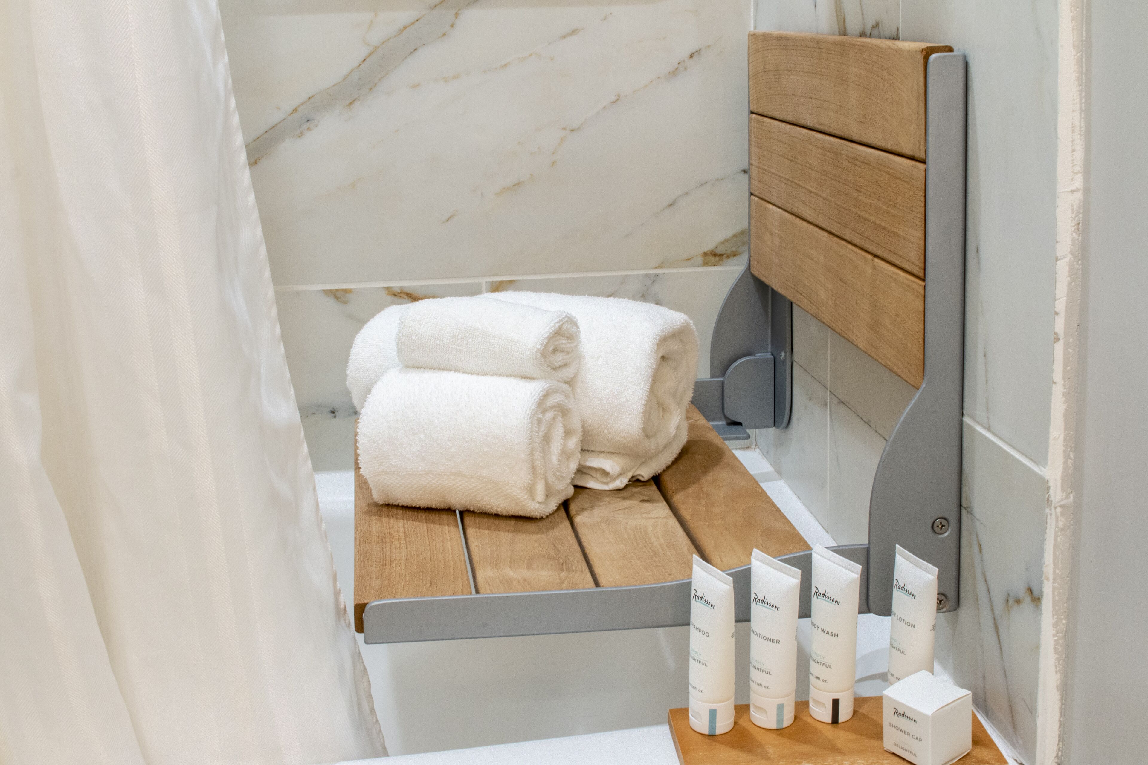 A bathroom with a wooden bench, two rolled towels, and a set of toiletries.