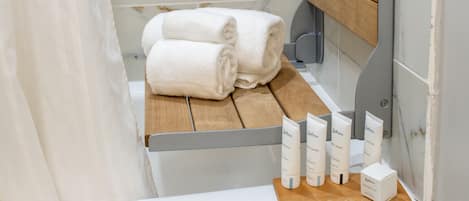 A bathroom with a wooden bench, two rolled towels, and a set of toiletries.