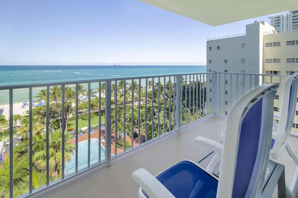 A balcony with a view of the ocean and a pool area.