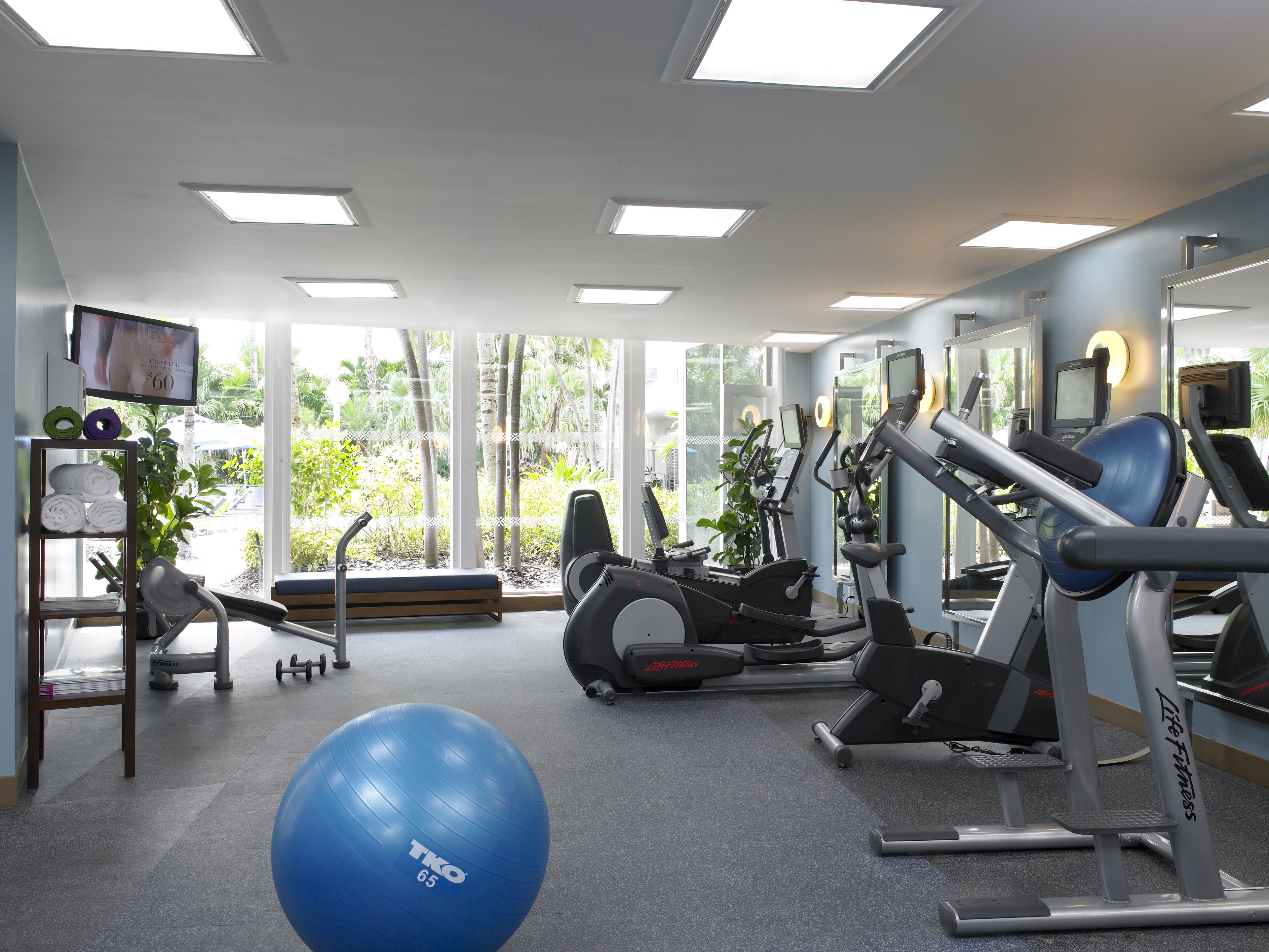 A gym with exercise equipment, a blue exercise ball, and a TV on the wall.