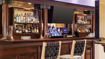 A bar area with wooden cabinets, shelves of liquor bottles, a flat-screen TV, and two patterned chairs.