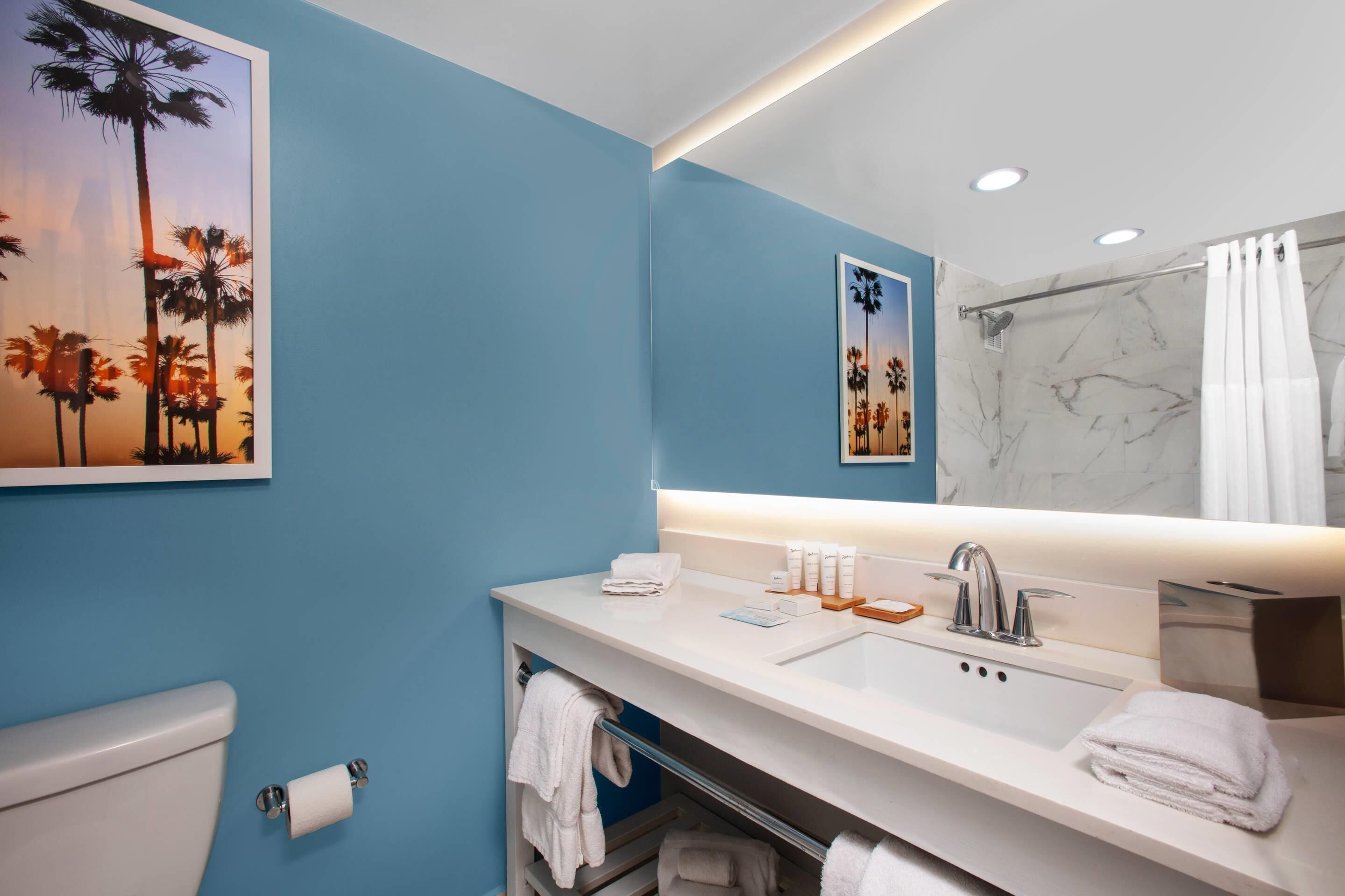 Ein Badezimmer mit blauer Wand, Waschbecken in Weiß, Spiegel und Toilette.