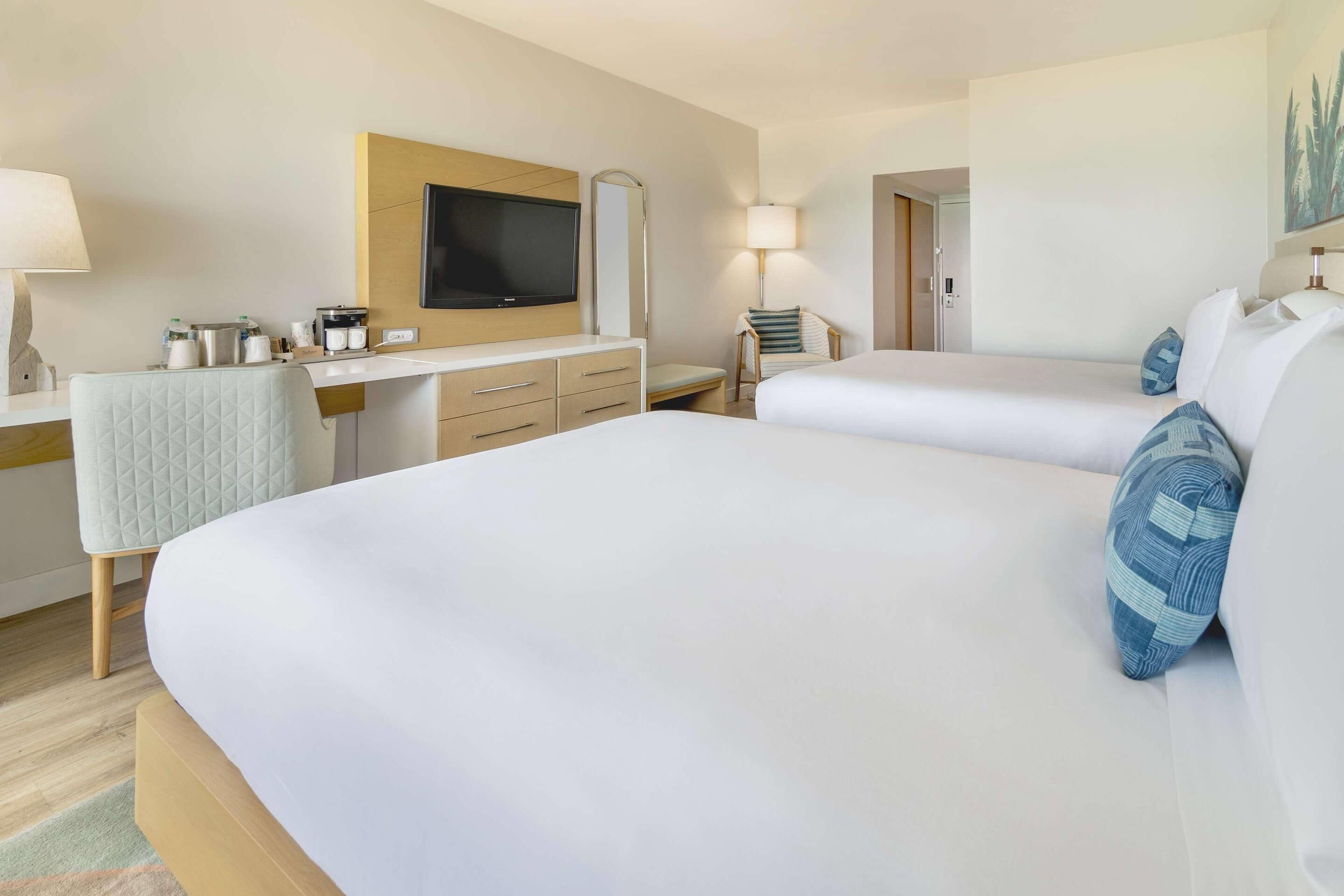 Une chambre d’hôtel avec deux lits, un bureau doté d’un téléviseur à écran plat, un miroir et une lampe.