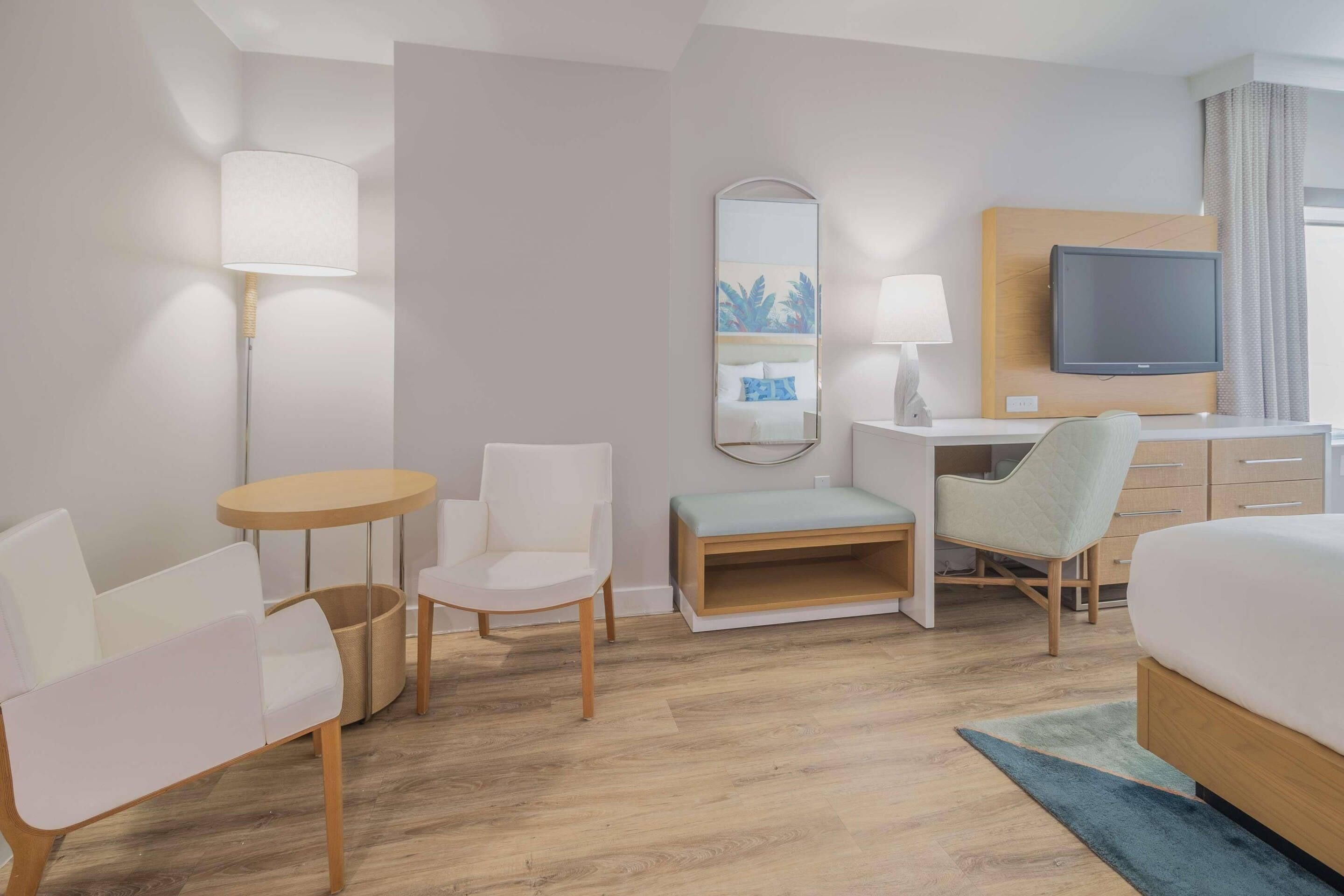 Ein Hotelzimmer mit Bett, Schreibtisch, zwei Stühlen, einem kleinen Tisch, Fernseher, Spiegel und Lampe.