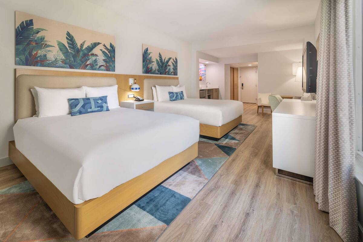 A hotel room with two beds, a desk, a chair, a bathroom, and a TV.