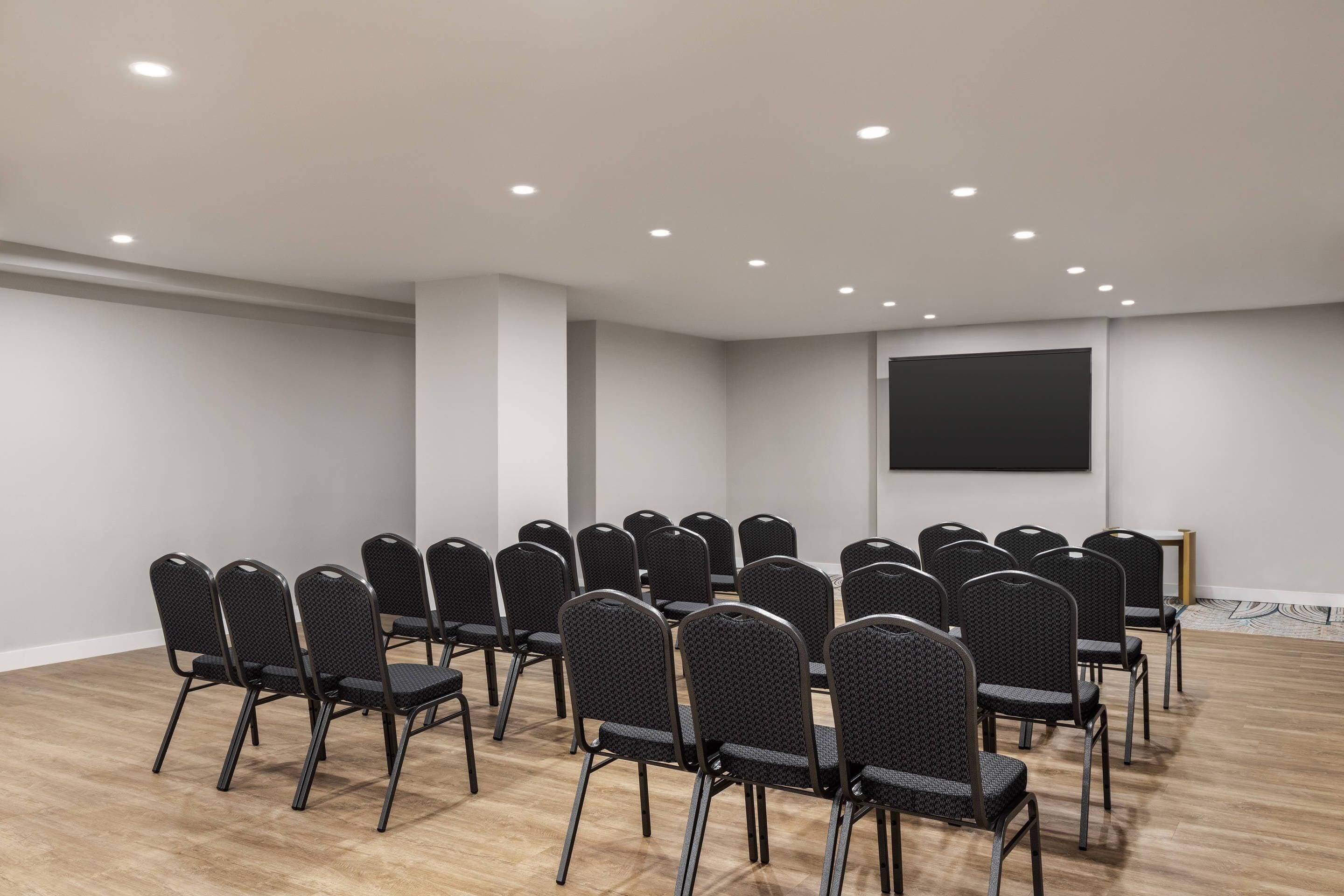 Une salle de conférence avec des rangées de chaises, un écran de projection et des spots encastrés au plafond.
