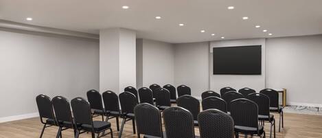 A conference room with rows of chairs, a projector screen, and recessed ceiling lights.