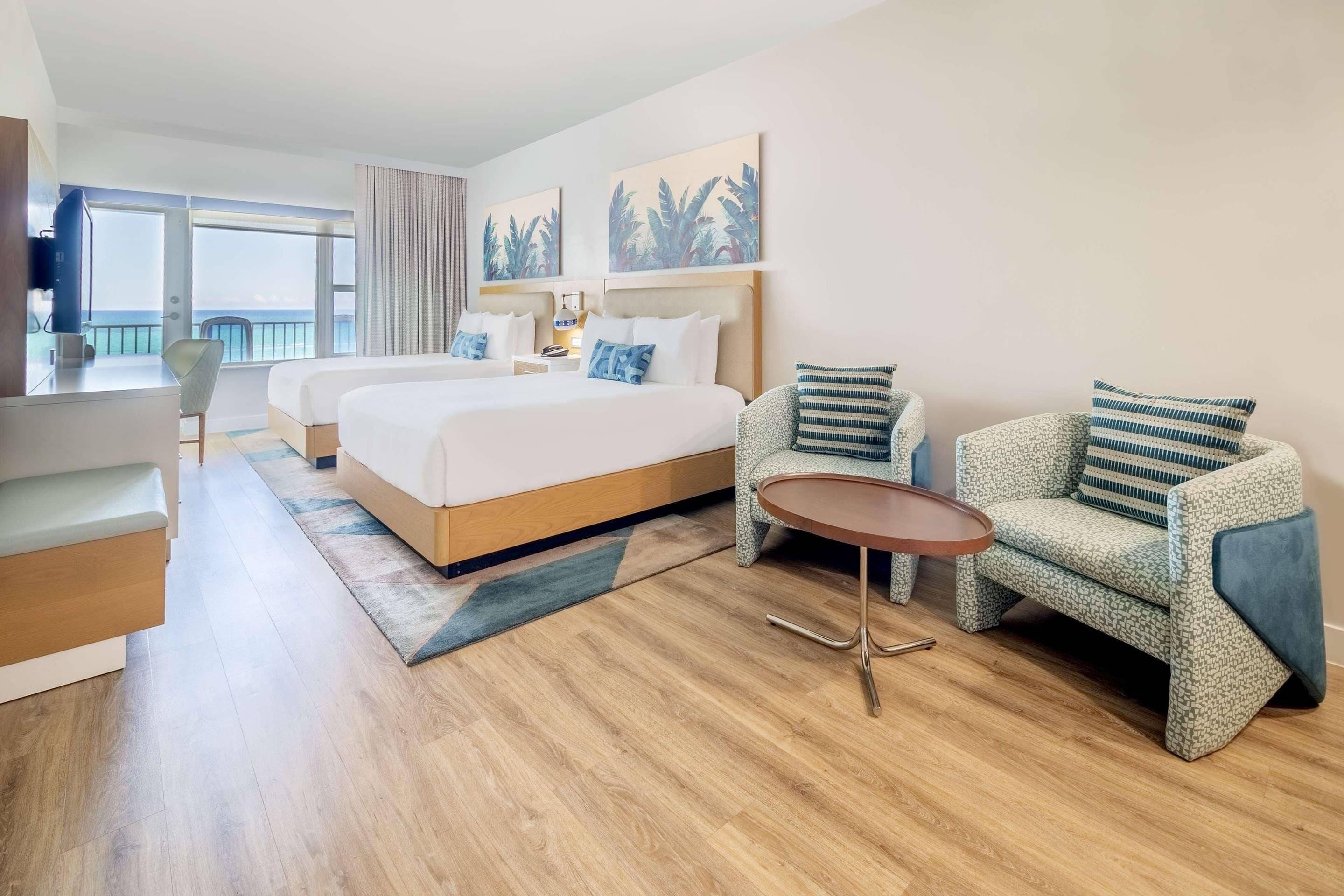 A hotel room with a bed, two chairs, a small table, and a TV.