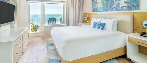 A hotel room with a large bed, a TV, a desk, and a view of the ocean.