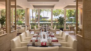 Comedor con mesas dispuestas para el servicio, ventanas amplias y vistas a palmeras.