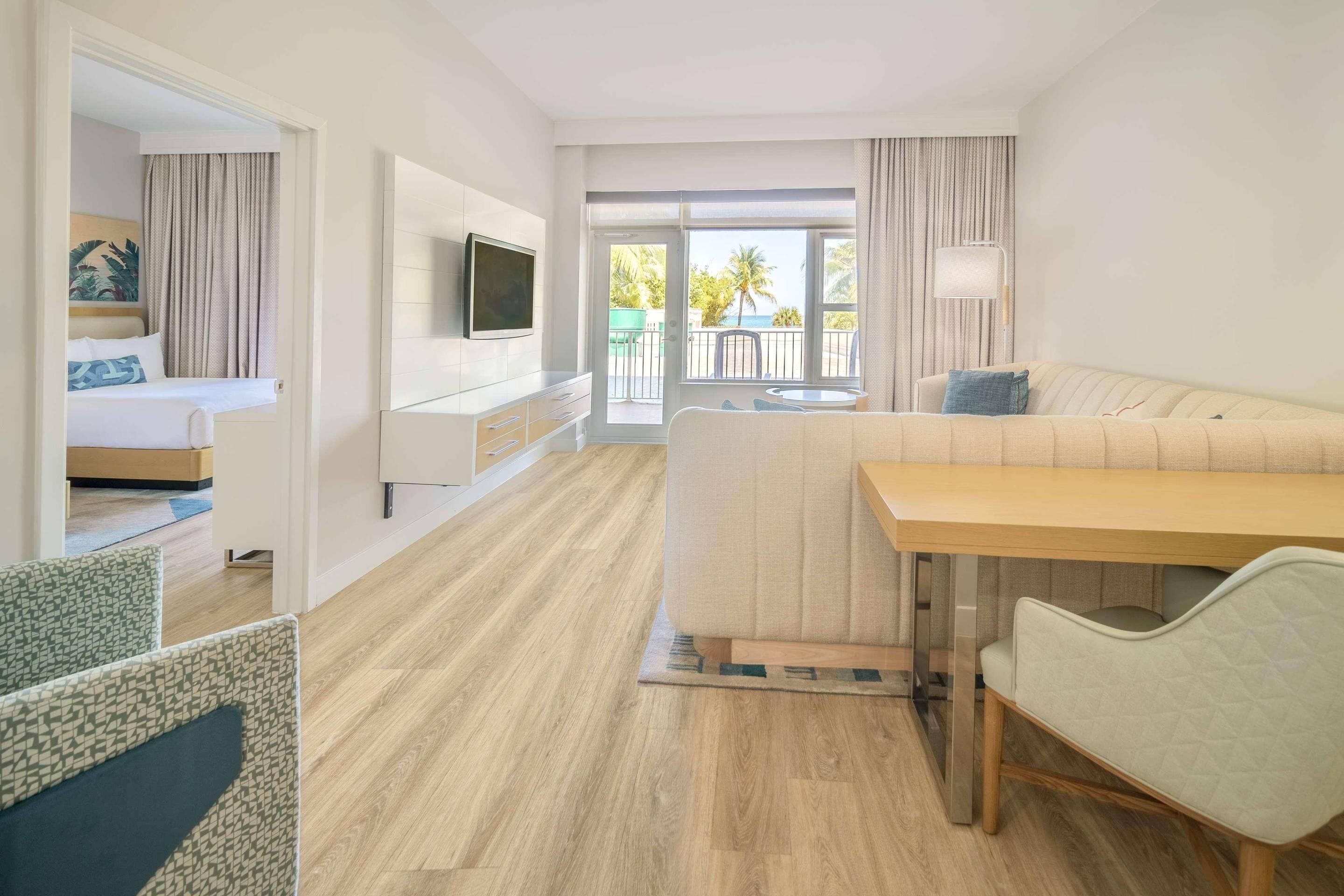 Ein Hotelzimmer mit Bett, einer Couch, einem Fernseher, einem Esstisch und einem Balkon mit Blick.