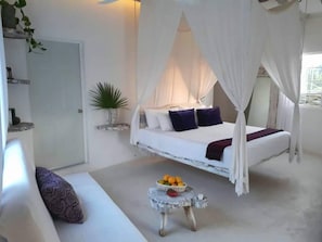A bedroom with a canopy bed, a small table with fruit, and a potted plant.