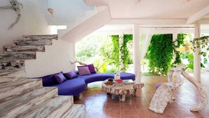 A modern living room with a curved sofa, a round coffee table, and a staircase with wooden steps. - Casa Del Viento (Isla Holbox)