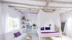 A bedroom with a bed under a canopy, a sofa, a small table with fruit, and a view of a bathroom. - Casa Del Viento (Isla Holbox)
