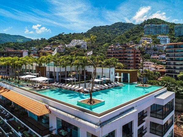 A rooftop swimming pool with lounge chairs and a view of a mountainous landscape.
