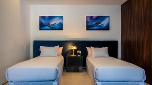 A hotel room with two beds, a nightstand with a lamp, and two paintings on the wall.