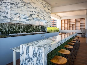 A modern bar area with a marble countertop, wooden stools, and a green vertical garden.