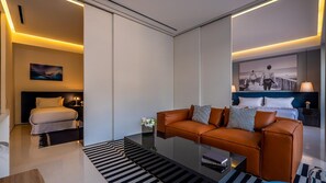 A modern hotel room with a sofa, a bed, a bedside table, and a large window.