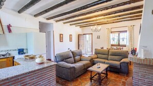 A living room with a sofa, a coffee table, and a kitchen area with a sink and cabinets. - Las Gallinas Órgiva by Ruralidays (Granada)
