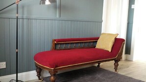 A room with a wooden bench with red upholstery, a grey rug, and a floor lamp.