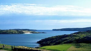 A coastal landscape with a clear sky, a sandy beach, and rocky terrain.