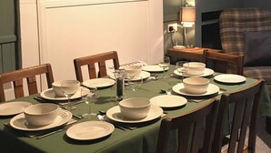 A dining table set for four with white plates and bowls, a green tablecloth, and a wooden chair.
