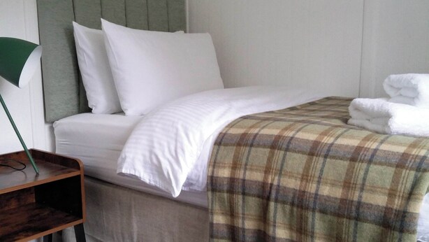 A neatly made bed with white linens, a plaid blanket, and a green headboard.