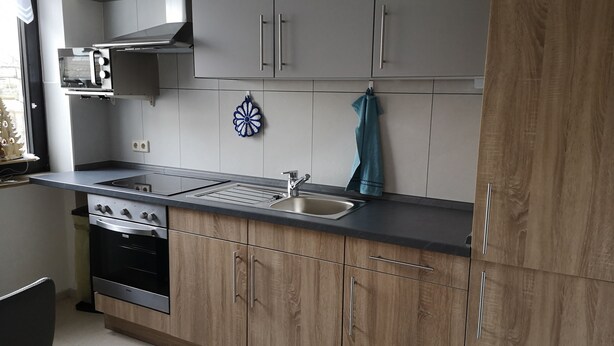 Een moderne keuken met grijze kastjes, een zwart aanrecht, een roestvrijstalen spoelbak en een ingebouwde oven.