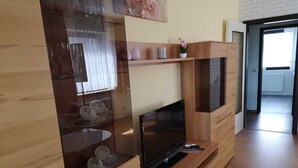 Een moderne woonkamer met een flatscreen televisie, houten meubels en een glazen kast met decoratieve objecten.