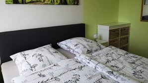 Een slaapkamer met een bed, nachtkastje, dressoir en een wanddecoratie met een bosmotief.